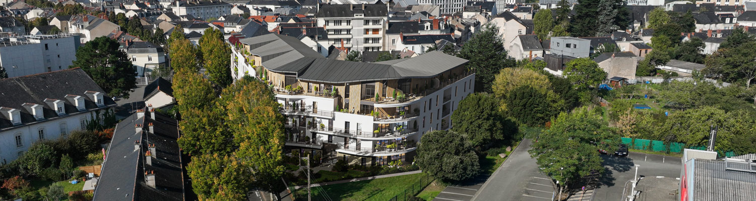 Ce projet présente une architecture moderne et intégrée à son environnement. Le bâtiment principal est un complexe résidentiel de plusieurs étages, caractérisé par des façades blanches avec des éléments de bardage en bois et des balcons incurvés et verdoyants. Il offre des terrasses spacieuses au dernier étage avec des finitions en bois. L'aménagement paysager est soigné, incluant des espaces verts collectifs et des arbres matures, suggérant un cadre de vie urbain mais aéré. L'ensemble s'insère dans un quartier résidentiel existant, comme le montre la vue aérienne.