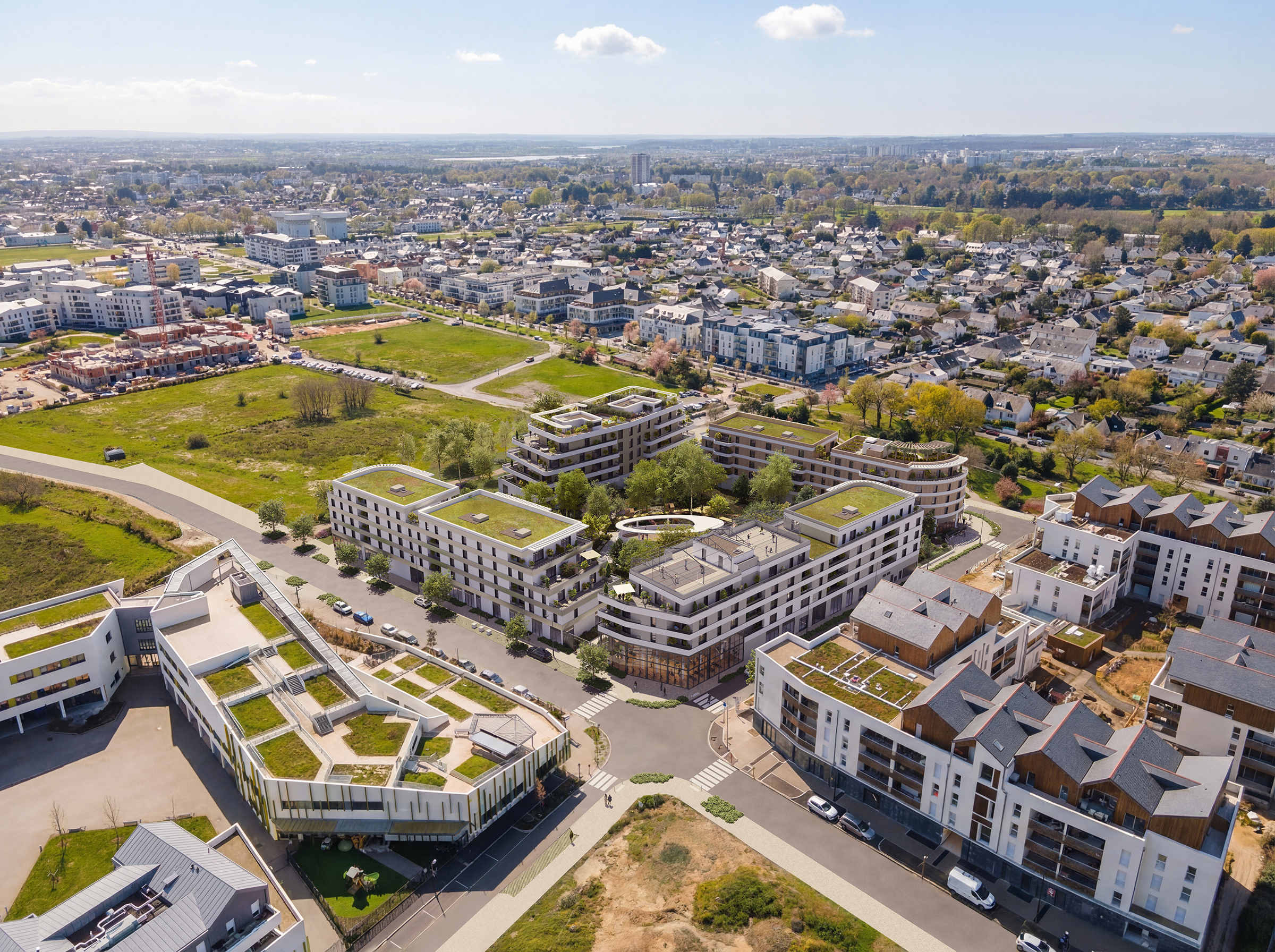 Cette vue aérienne diurne offre un panorama complet du projet immobilier, révélant un ensemble résidentiel moderne parfaitement intégré dans son environnement urbain et paysager. Les différents bâtiments, reconnaissables à leurs toitures végétalisées et à leurs lignes architecturales blanches et épurées, s'organisent autour d'un cœur d'îlot arboré et de cheminements piétons structurés. L'image met en avant la densité maîtrisée de l'opération, qui fait la transition entre des zones pavillonnaires plus traditionnelles à l'arrière-plan et des infrastructures collectives contemporaines au premier plan. L'ensoleillement et la clarté du visuel soulignent la qualité des espaces extérieurs et la fluidité des axes de circulation qui desservent cette nouvelle pièce urbaine.